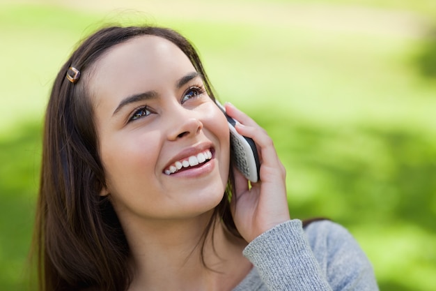 Młoda uśmiechnięta kobieta przyglądająca up podczas gdy opowiadający na telefonie