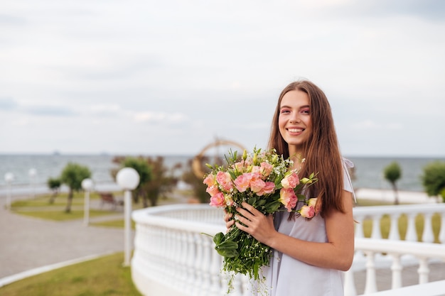 Młoda uśmiechnięta kobieta trzyma bukiet kwiatów w ręku na świeżym powietrzu na tarasie