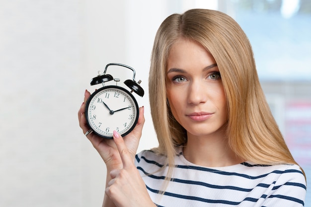 Młoda uśmiechnięta kobieta trzyma czerń zegar