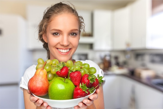 Młoda uśmiechnięta kobieta trzyma miskę ze świeżymi owocami, zdrowy tryb życia