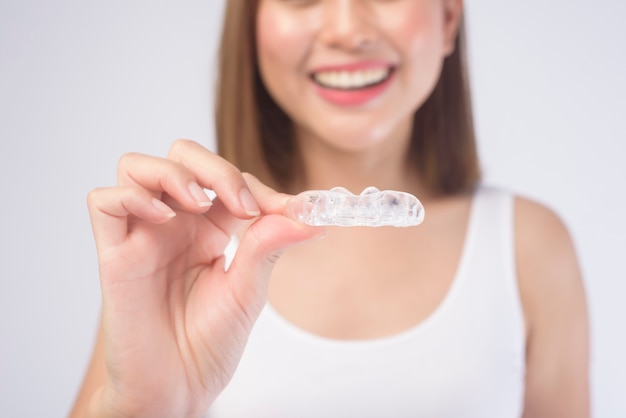 Młoda uśmiechnięta kobieta trzyma szelki invisalign na białym, opieki stomatologicznej i koncepcji ortodontycznej.