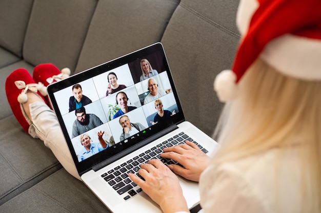 Młoda uśmiechnięta kobieta w czerwonym kapeluszu Świętego Mikołaja podczas rozmowy wideo w sieci społecznościowej z rodziną i przyjaciółmi w Boże Narodzenie.
