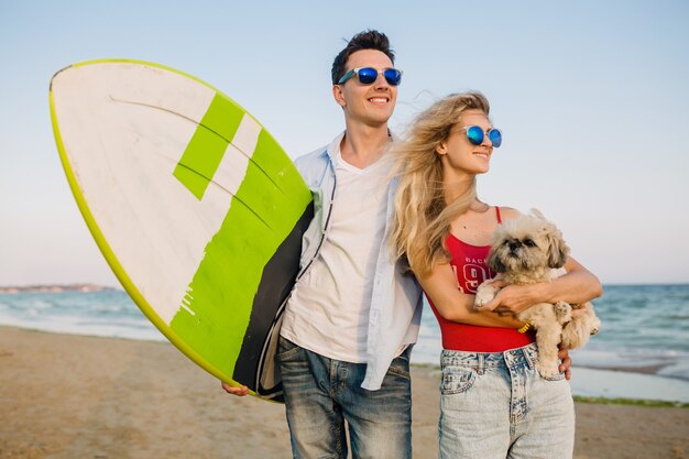 Młoda Uśmiechnięta Para Bawi Się Na Plaży Pozuje Z Deską Surfingową Bawiąc Się Z Psem