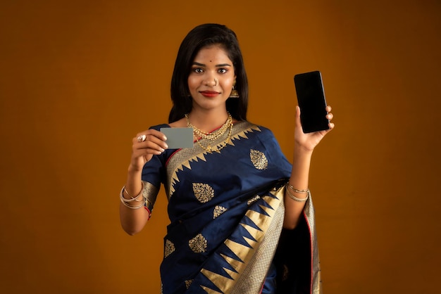 Młoda uśmiechnięta piękna kobieta lub dziewczyna przedstawiająca kartę kredytową podczas korzystania z telefonu komórkowego lub smartfona