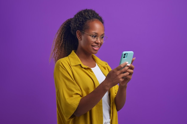 Młoda wesoła Afroamerykanka trzymająca smartfon stoi w studio