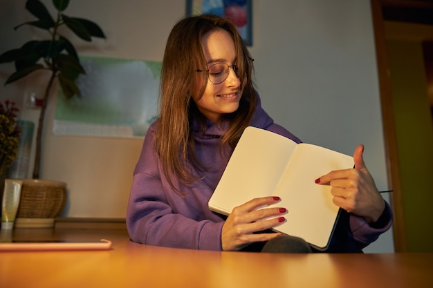 Młoda wesoła, pewna siebie i szczęśliwa freelancerka pracuje wieczorem na laptopie w domu