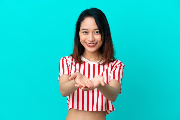 Młoda Wietnamka odizolowana na niebieskim tle trzyma wyimaginowaną copyspace na dłoni, aby wstawić reklamę