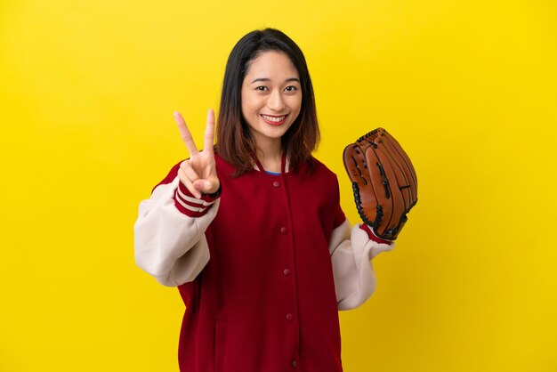 Młoda wietnamska kobieta w rękawiczce baseballowej na żółtym tle, uśmiechnięta i pokazująca znak zwycięstwa