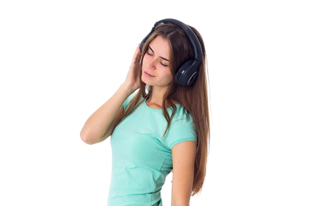 Młoda wspaniała kobieta w niebieskiej koszulce i czarnych słuchawkach na białym tle w studio