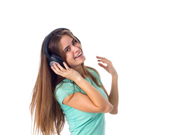 Młoda wspaniała kobieta w niebieskiej koszulce słuchająca muzyki w czarnych słuchawkach na białym tle w studio