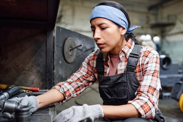 Młoda współczesna kobieta w odzieży roboczej wybierająca metalowe części zamienne