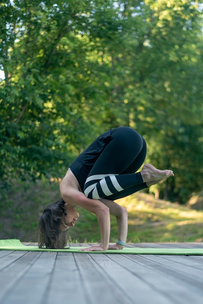 Młoda wysportowana kobieta ćwiczy jogę w parku w pozie żurawia Instruktor Bakasana Yoga podczas treningu