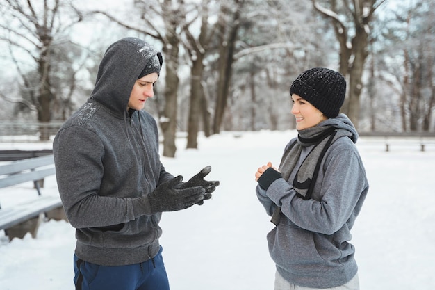 Młoda wysportowana para rozmawia w zaśnieżonym parku miejskim po zimowym treningu joggingowym