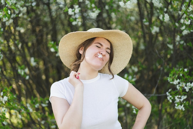 Młoda zabawna piękna kobieta w kapeluszu wśród kwitnących drzew oddycha wolna szczęśliwa kobieta bez alergii