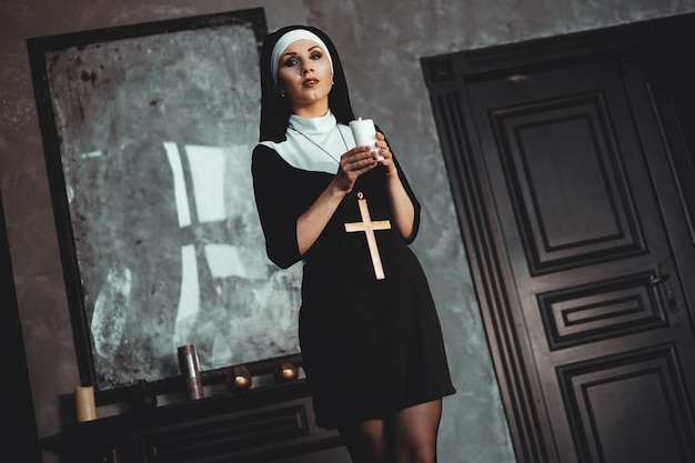 Młoda zakonnica katolicka trzyma świecę w dłoniach. Zdjęcie na czarnym tle. Portret pięknej kobiety