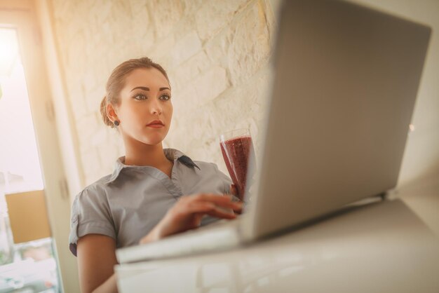 Młoda zamyślona kobieta na przerwie w kawiarni. Pracuje przy laptopie.