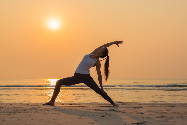 Młoda zdrowa joga kobiety ćwiczy joga poza na plaży przy wschodem słońca