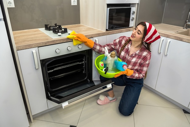 Młoda żona czyszczenia piekarnika żółtą szmatą i sprayem w kuchni.