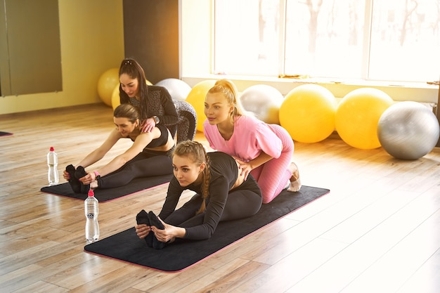 Młode aktywne kobiety o szczupłym ciele wykonujące ćwiczenia rozciągające, aby zachować elastyczność ciała na macie do jogi