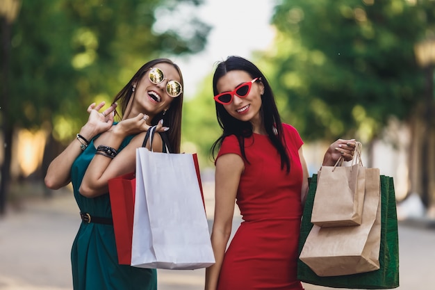 Młode atrakcyjne dziewczyny z torby na zakupy w mieście lato. Piękne kobiety w okularach przeciwsłonecznych i uśmiechnięte. Pozytywne emocje i koncepcja dzień zakupów.