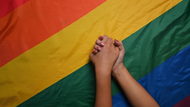 Młode azjatyckie kobiety LGBT para lesbijek trzymające się za ręce nad flagą dumy LGBT