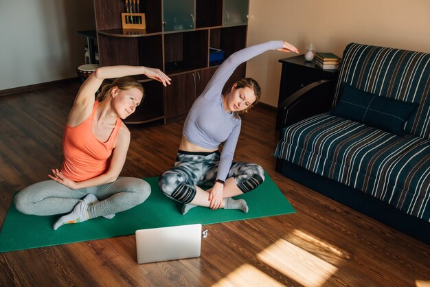 Młode Dziewczyny Robią ćwiczenia Fitness Za Pomocą Internetowych Programów Szkoleniowych Na Laptopie