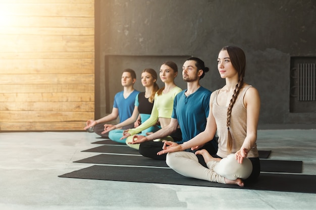 Młode kobiety i mężczyźni na zajęciach jogi, ćwiczenia medytacyjne. Lotos pozuje do relaksu. Zdrowy styl życia w klubie fitness, kopia przestrzeń