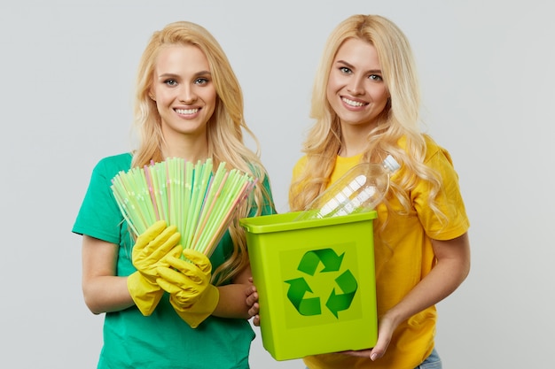 Zdjęcie młode kobiety ochotniczki w żółtych i zielonych koszulkach i rękawiczkach zbierają odpady z tworzyw sztucznych w pojemniku w celu recyklingu.