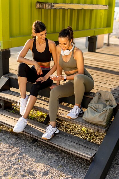 Młode kobiety w strojach sportowych patrzące na telefon komórkowy po treningu