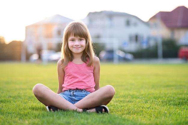 Młode ładne dziecko dziewczyna siedzi na świeżym zielonym trawniku w ciepły letni dzień na zewnątrz