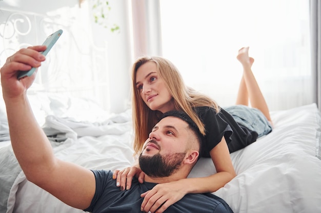 Młode małżeństwo co selfie za pomocą telefonu w sypialni w ciągu dnia.