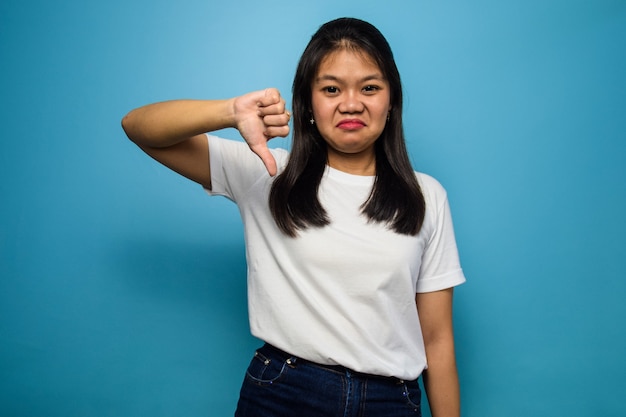Młode piękne azjatyckie kobiety używają białej koszulki z niebieskim odosobnionym gestem kciuka w dół