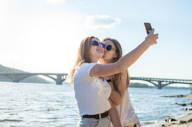 Młode piękne dziewczyny na plaży za pomocą smartfona robią sobie selfie