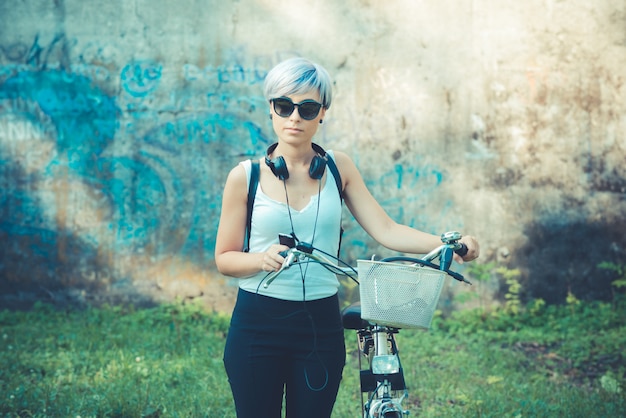 Zdjęcie młode piękne krótkie niebieskie włosy hipster kobieta ze słuchawkami i rower