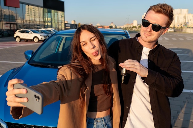 Młode, piękne małżeństwo robi sobie selfie przy zakupionym samochodzie na zewnątrz