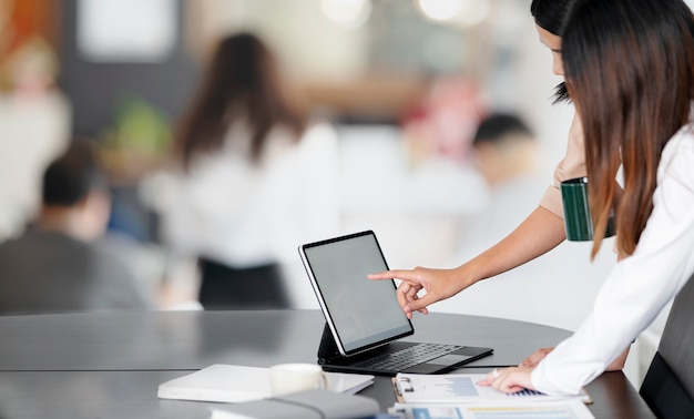 Młode samice ludzi biznesu pracujących razem na komputerze typu tablet w nowoczesnym biurze.