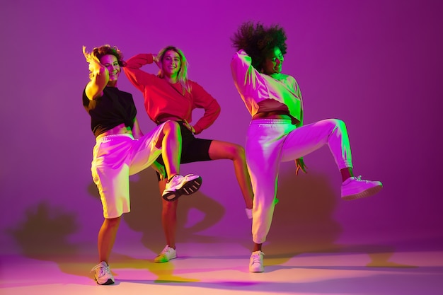 Młode sportowe dziewczyny tańczą hiphop w stylowych ubraniach na fioletoworóżowym tle w tańcu