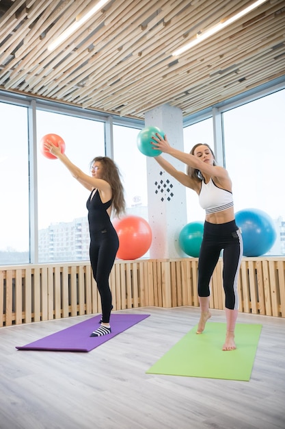 Młode szczupłe kobiety robiące ćwiczenia trzymające piłkę w studio fitness