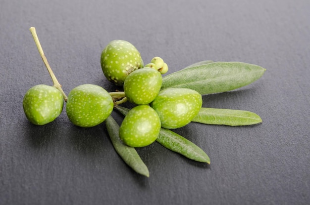 Młode zielone oliwki z liśćmi na czarnym tle