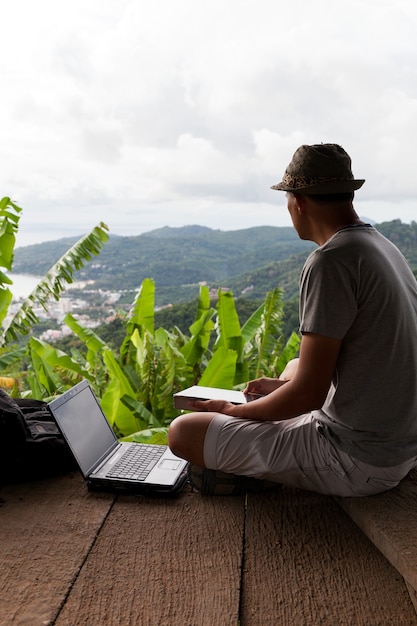 Zdjęcie młodego człowieka obsiadanie używać laptop przeciw sceneria krajobrazowemu lasowi i andaman morzu w phuket