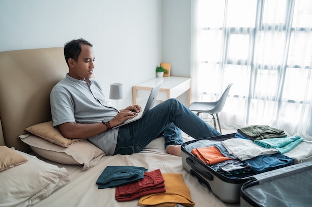 Młodego człowieka podróżnik używa laptop z walizką pełną odziewa