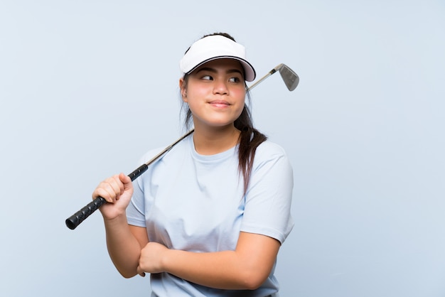 Młodego Golfisty Azjatycka Dziewczyna Nad Odosobnioną Błękit ścianą Robi Wątpliwość Gestowi Podczas Gdy Podnoszący Ramiona