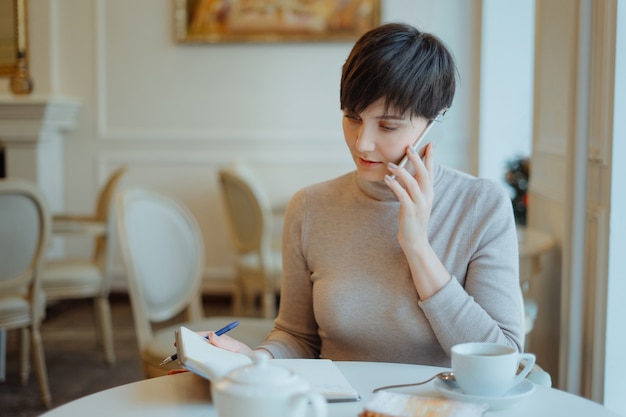 Młodego piękna uśmiechnięty kobiety obsiadanie w kawiarni i opowiadać na telefonie komórkowym