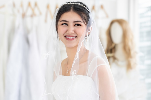 Młodej kobiety Azjatycki ono uśmiecha się i próbuje na ślubnej sukni w sklepie.