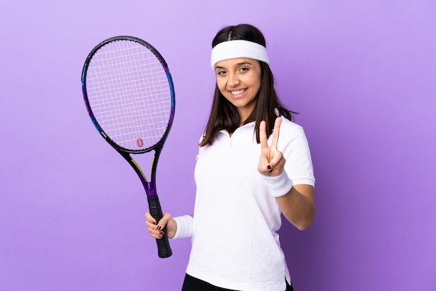 Młodej kobiety gracz w tenisa nad ścianą uśmiecha się zwycięstwo znaka i pokazuje