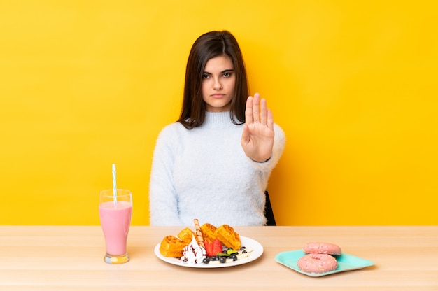 Młodej kobiety łasowania gofry i milkshake w stole nad odosobnionym kolorem żółtym