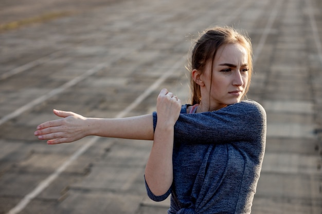 Zdjęcie młodej kobiety szkolenie na stadium w lecie. sportsmenka, rozciąganie, rozgrzewka przed ćwiczeniami na zewnątrz. zdrowy tryb życia