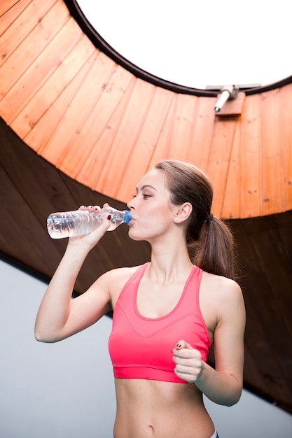 Młodej kobiety woda pitna od butelki w gym