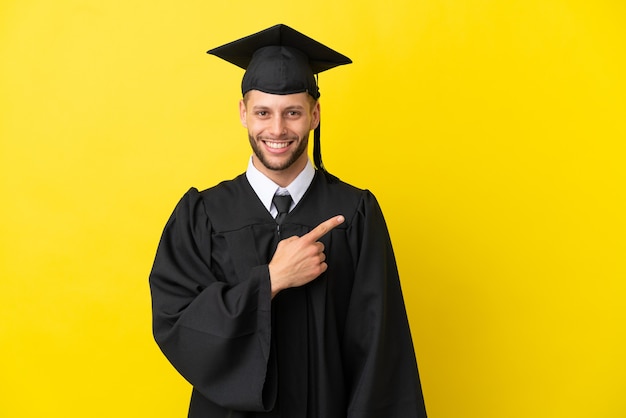 Młody absolwent uniwersytetu kaukaski mężczyzna odizolowany na żółtym tle wskazujący na bok, aby zaprezentować produkt