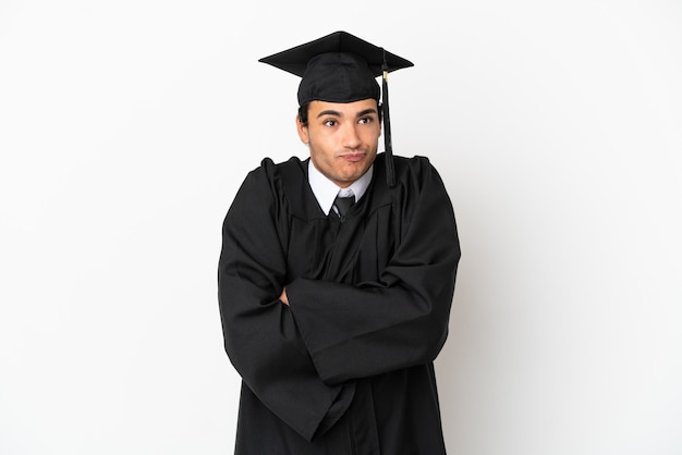 Młody absolwent uniwersytetu na białym tle robi gest wątpliwości podczas podnoszenia ramion